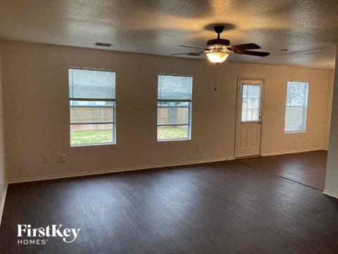 an empty living room with a ceiling fan and three windows