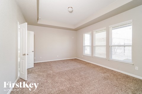 a spacious living room with carpet and three windows