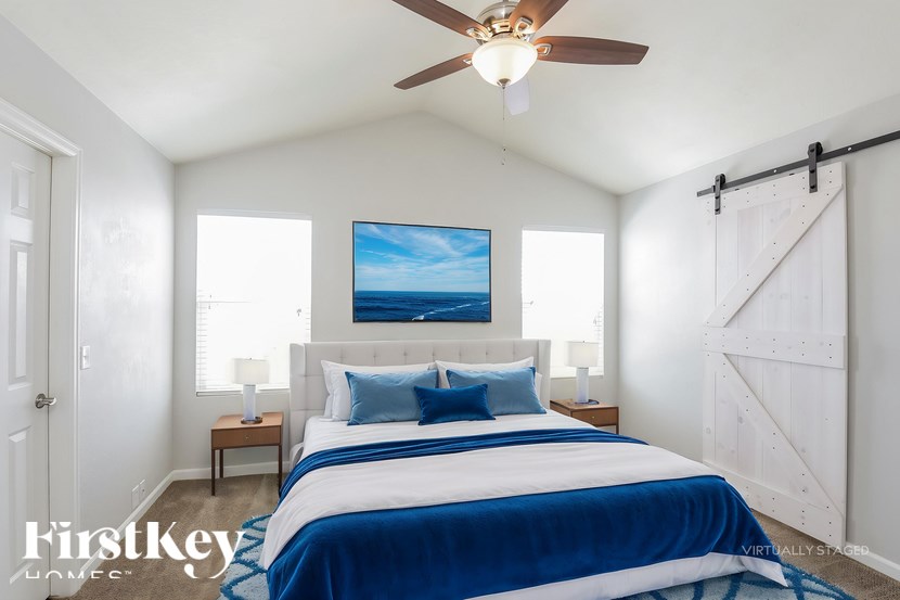 A bedroom with a bed, a ceiling fan, and a painting on the wall.