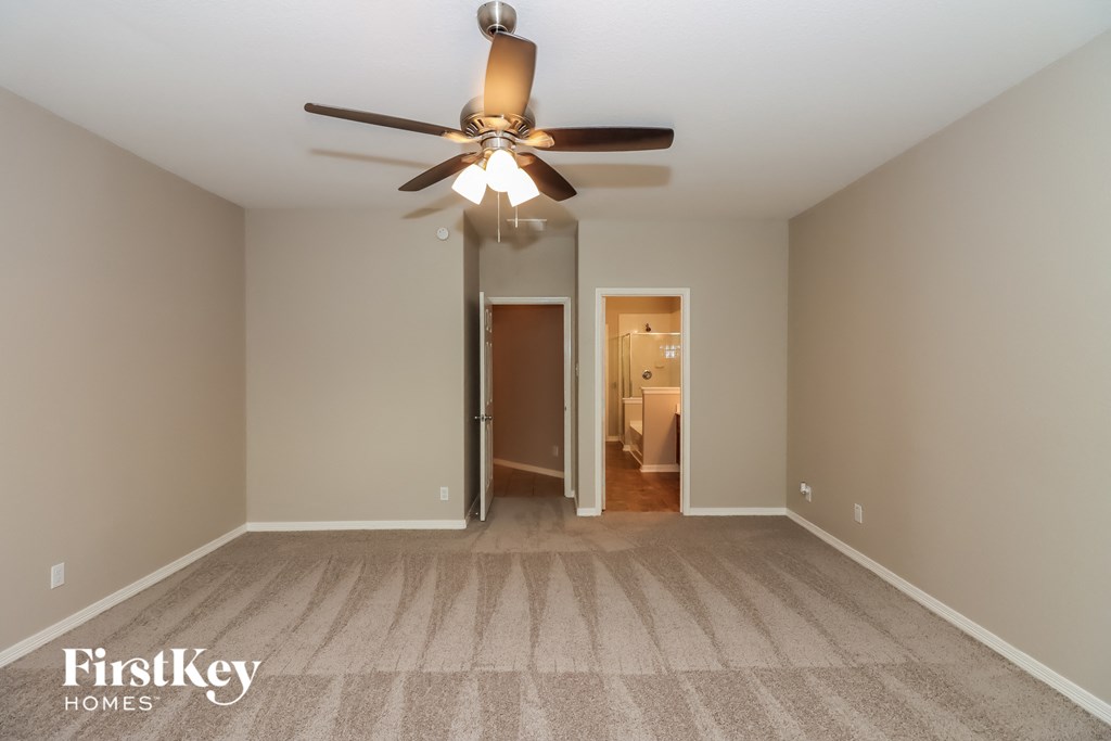 an empty living room with a ceiling fan and a door to a bathroom
