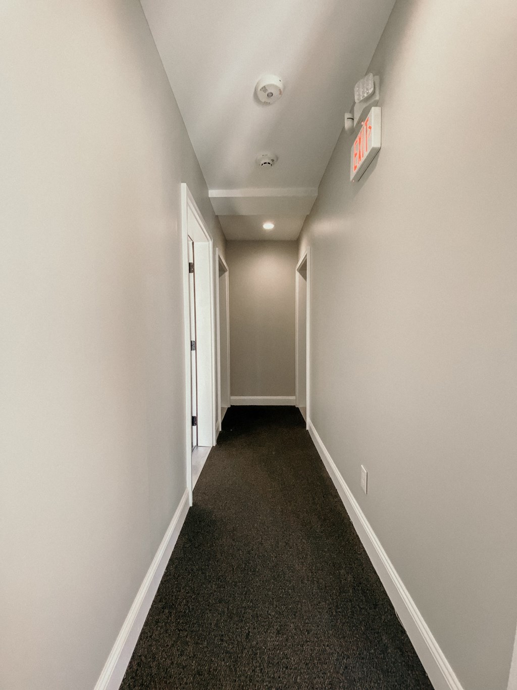 a long hallway with gray carpet and white walls and a exit sign