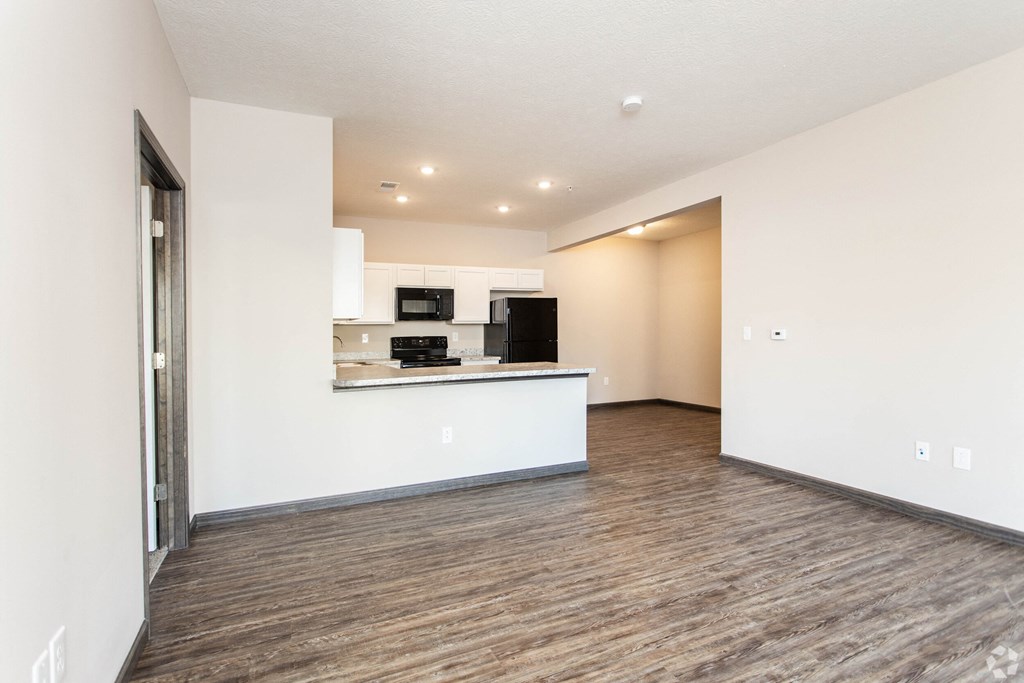 the living room and kitchen of an apartment with white walls and wood flooring