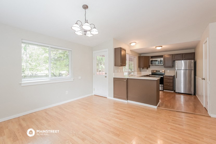 an empty living room with a kitchen with stainless steel appliances