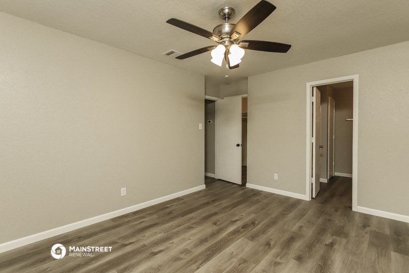 the spacious living room with ceiling fan and hallway to the bedroom