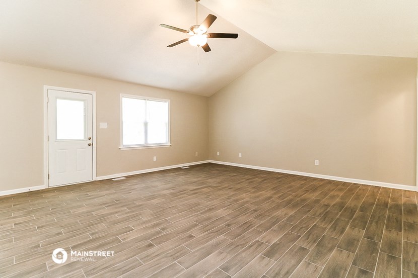 the spacious living room with wood flooring and a ceiling fan