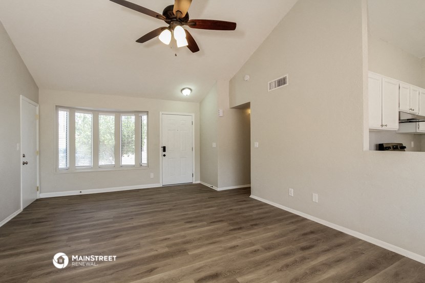 the spacious living room with ceiling fan and white walls