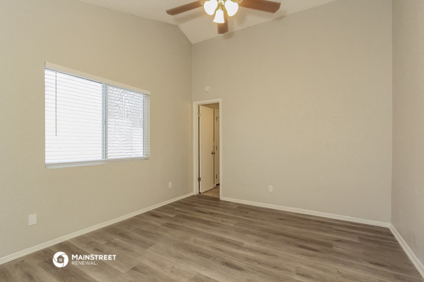 the spacious living room with wood flooring and a ceiling fan