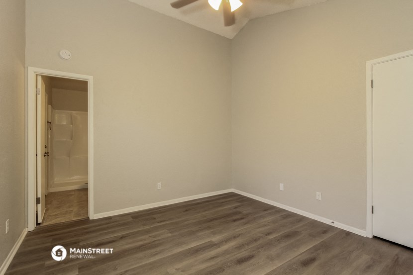 the spacious living room with wood flooring and a ceiling fan