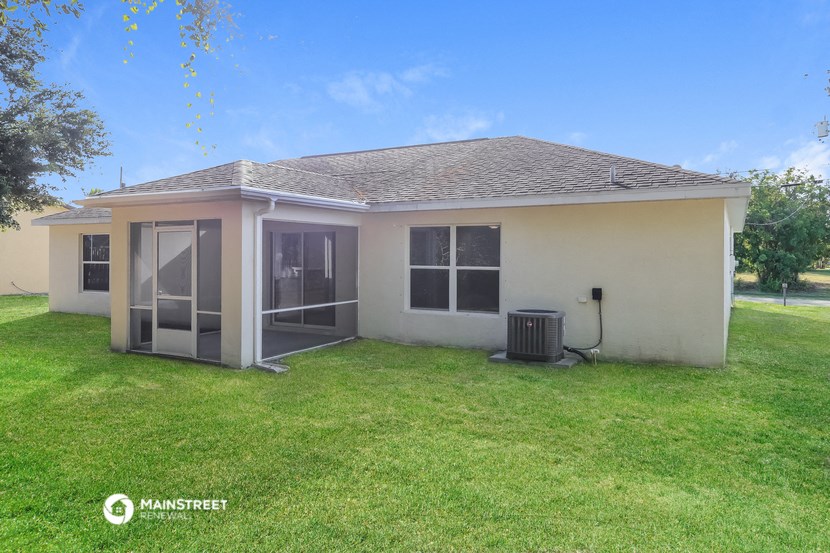 the backyard of a small house with a yard and a trash can
