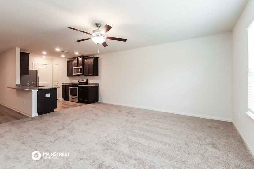 an empty living room and kitchen with a ceiling fan