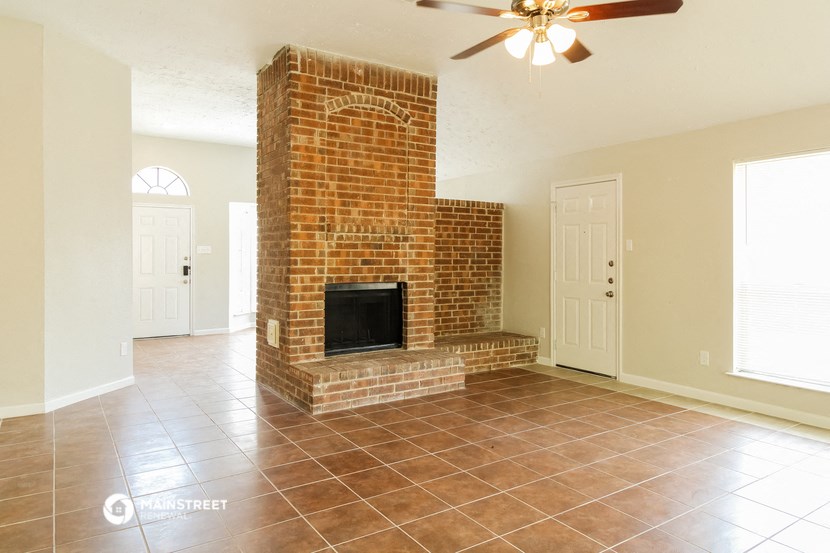 an empty living room with a brick fireplace and tile flooring