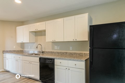 a kitchen with white cabinets and granite counter tops and a black refrigerator