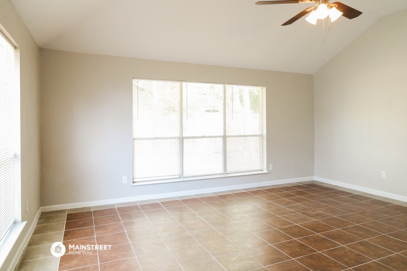 an empty living room with a large window and a ceiling fan