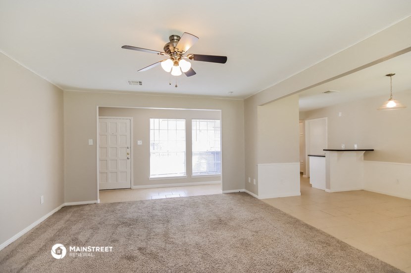 an empty living room with a ceiling fan and a kitchen