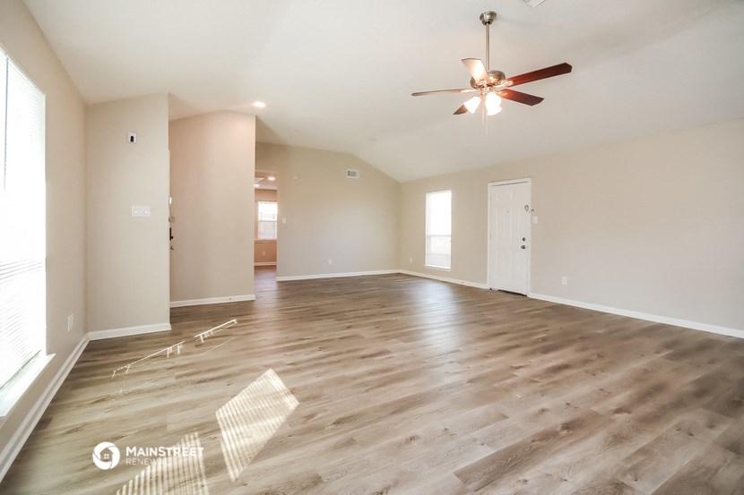 the spacious living room with hardwood floors and a ceiling fan