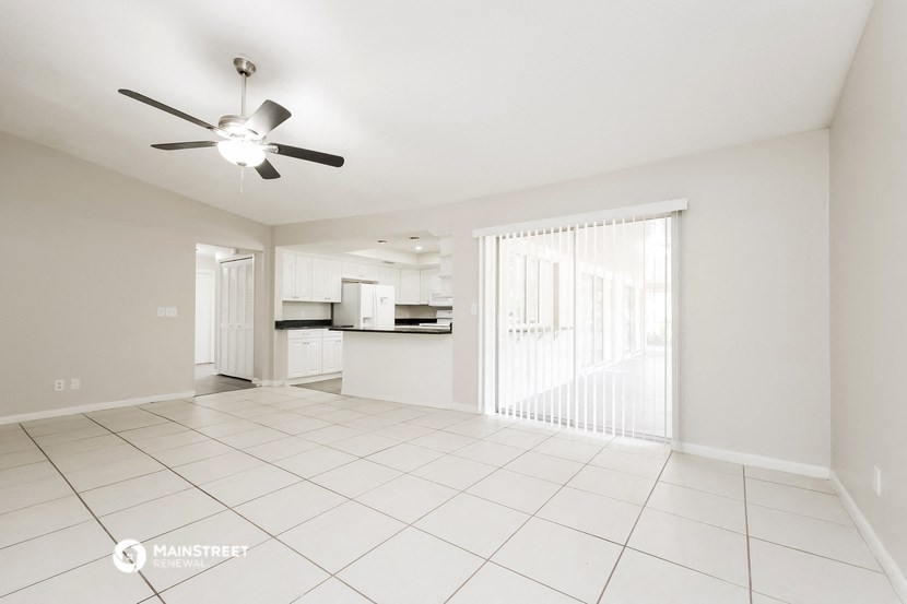 an empty living room with a kitchen and a ceiling fan