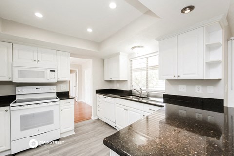 a white kitchen with black counter tops and white appliances