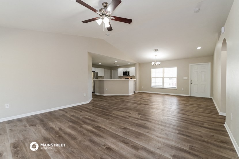 an empty living room with a ceiling fan and a kitchen