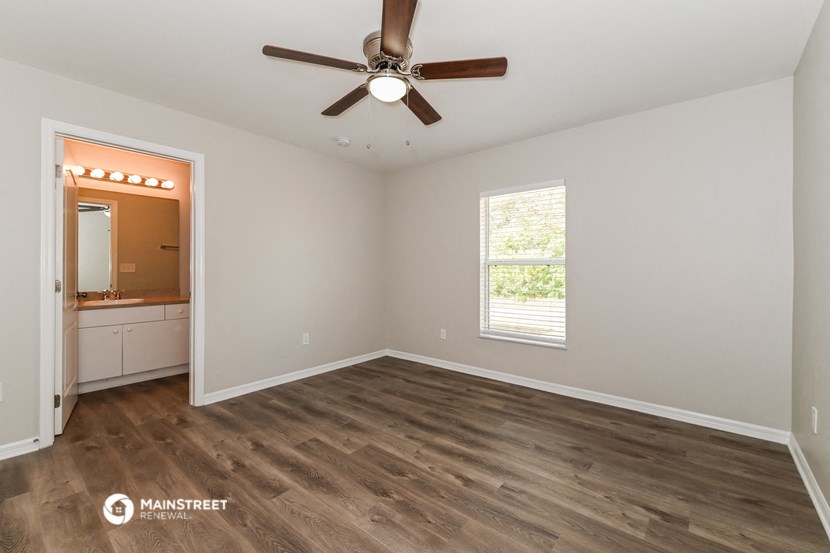 the spacious living room with wood flooring and a ceiling fan