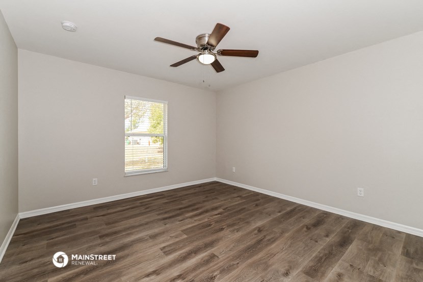 the spacious living room with wood flooring and a ceiling fan