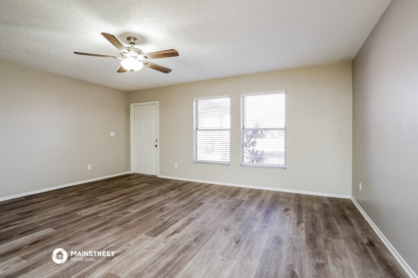 the spacious living room with wood flooring and a ceiling fan