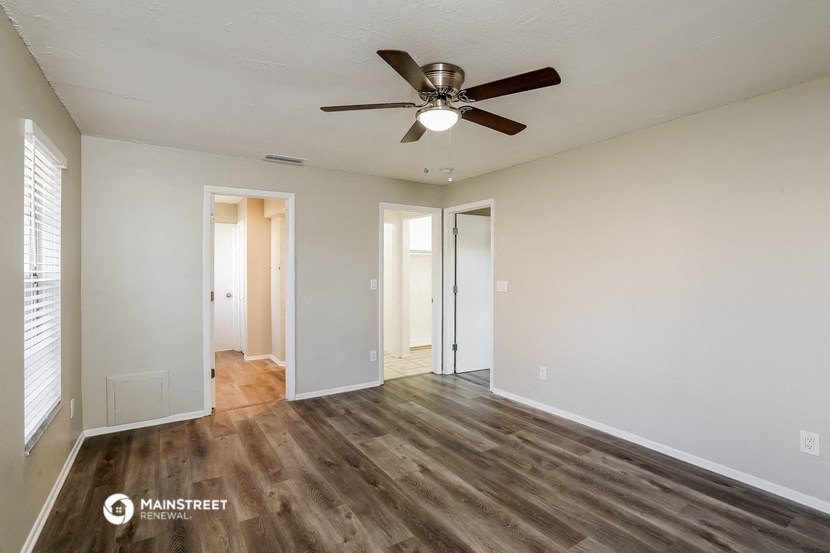 the spacious living room with ceiling fan and white walls