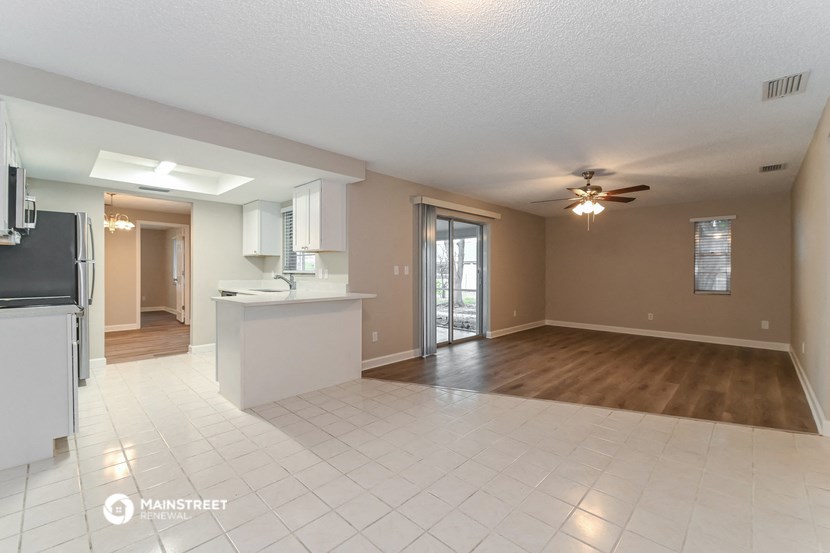 an empty living room with a kitchen and a ceiling fan