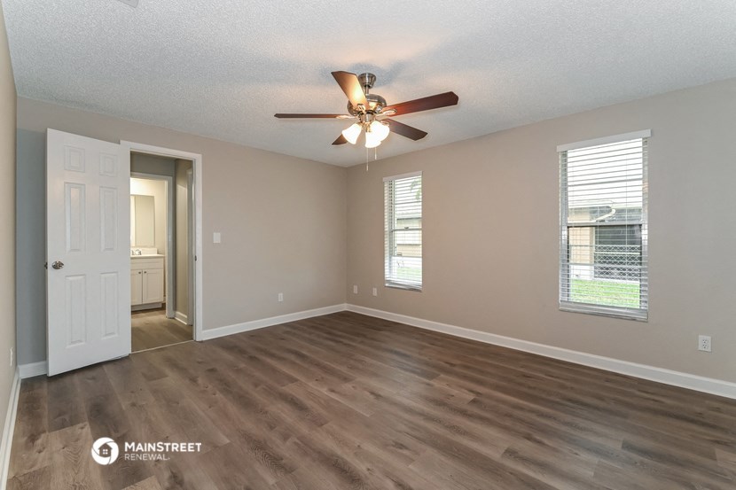 an empty living room with a ceiling fan and a door to a bathroom