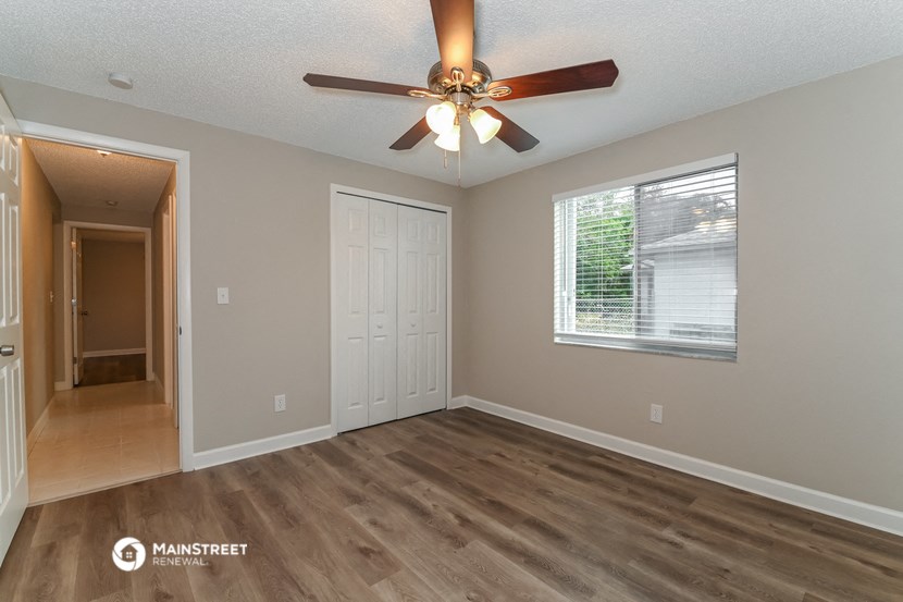 the spacious living room with a ceiling fan and a door to the hallway