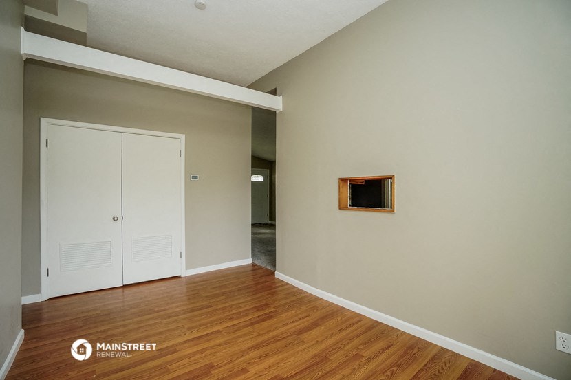 an empty living room with wood floors and a door to a hallway