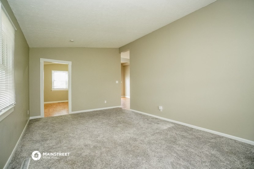 the living room of an empty house with carpet and a window