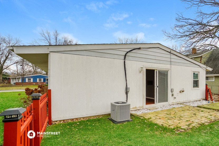 the backyard of a small white house with a red fence