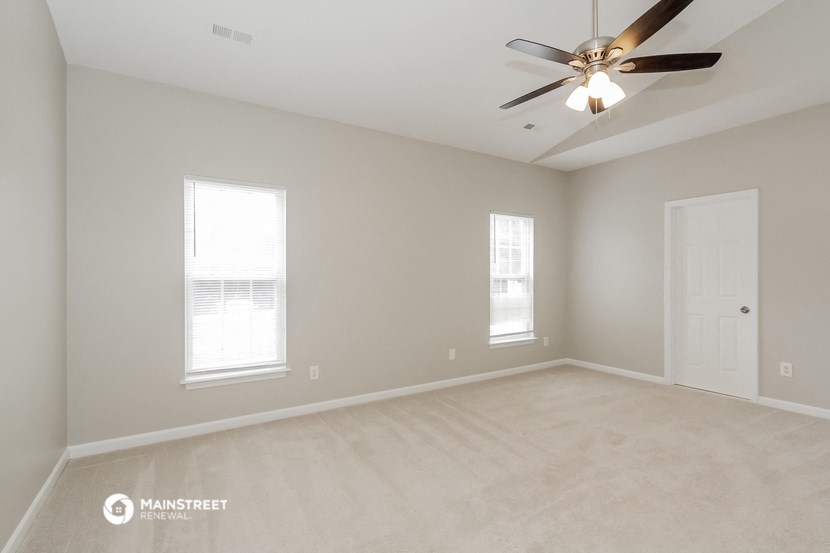 the spacious living room with ceiling fan and two windows