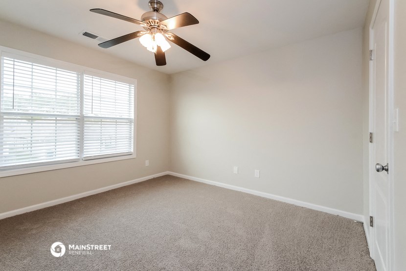 the spacious living room with ceiling fan and large window