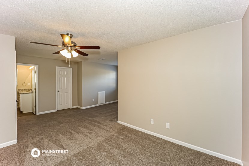 the living room is spacious with carpet and a ceiling fan