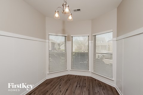 A room with wooden floors and white walls, featuring a window with blinds and a chandelier.