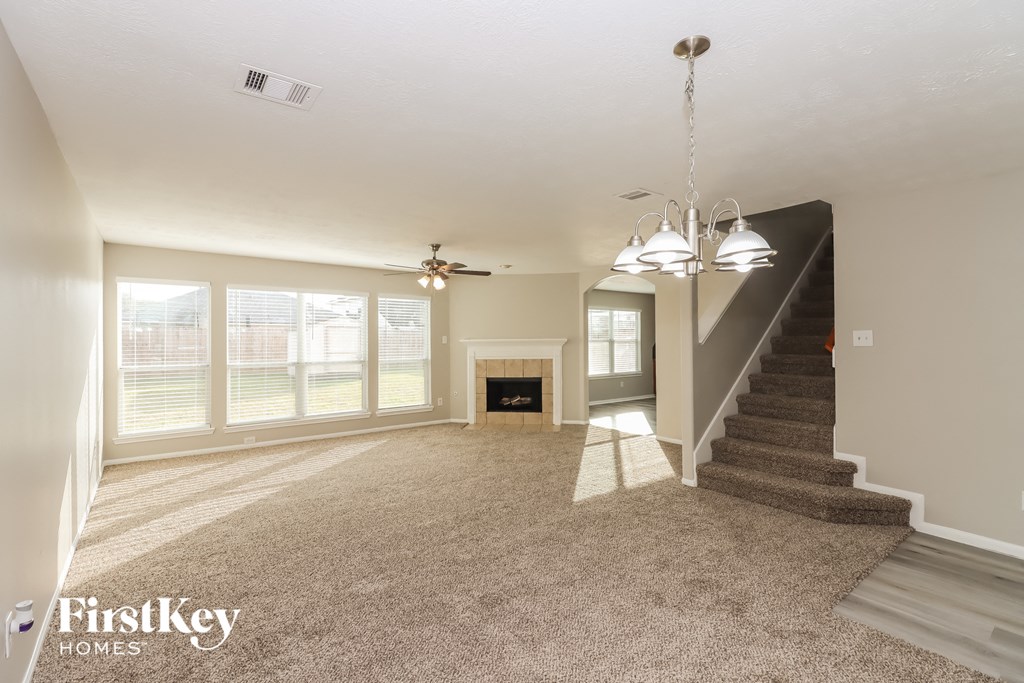 an empty living room with a fireplace and a carpeted staircase