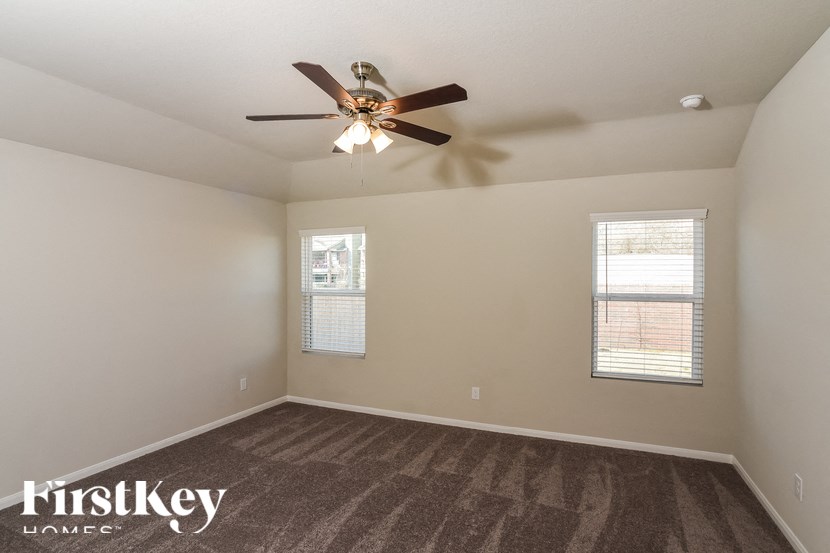 A room with a carpeted floor, a ceiling fan, and two windows.
