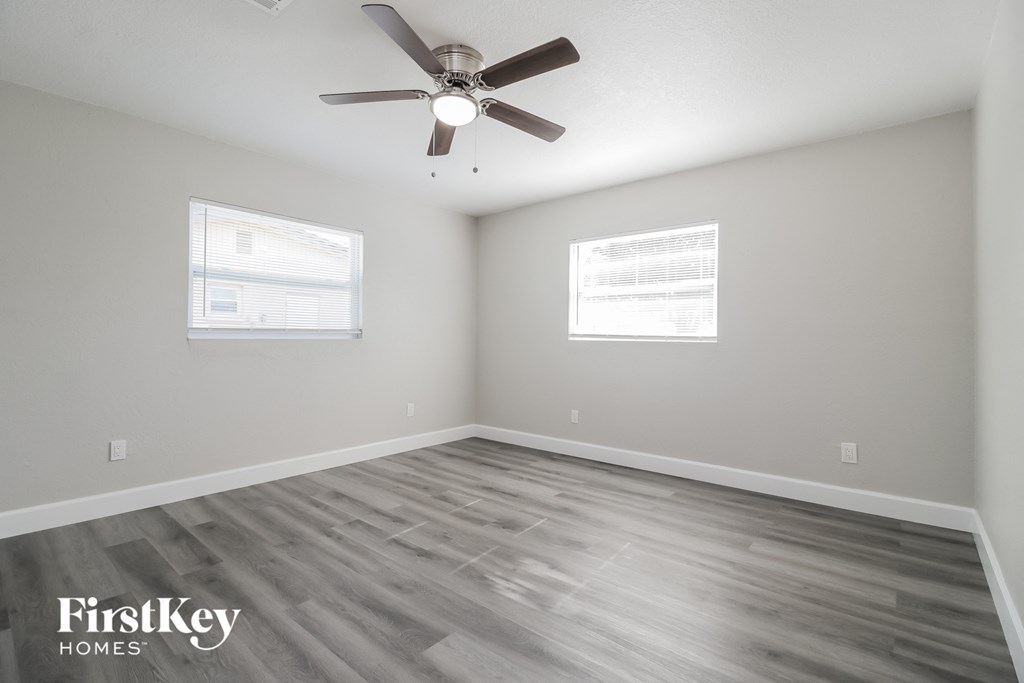 A room with a ceiling fan and two windows.