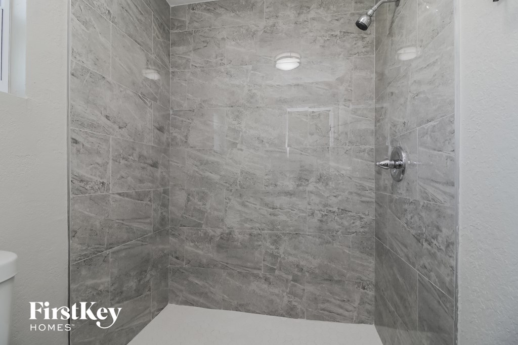 A bathroom with a grey tiled shower and a white toilet.