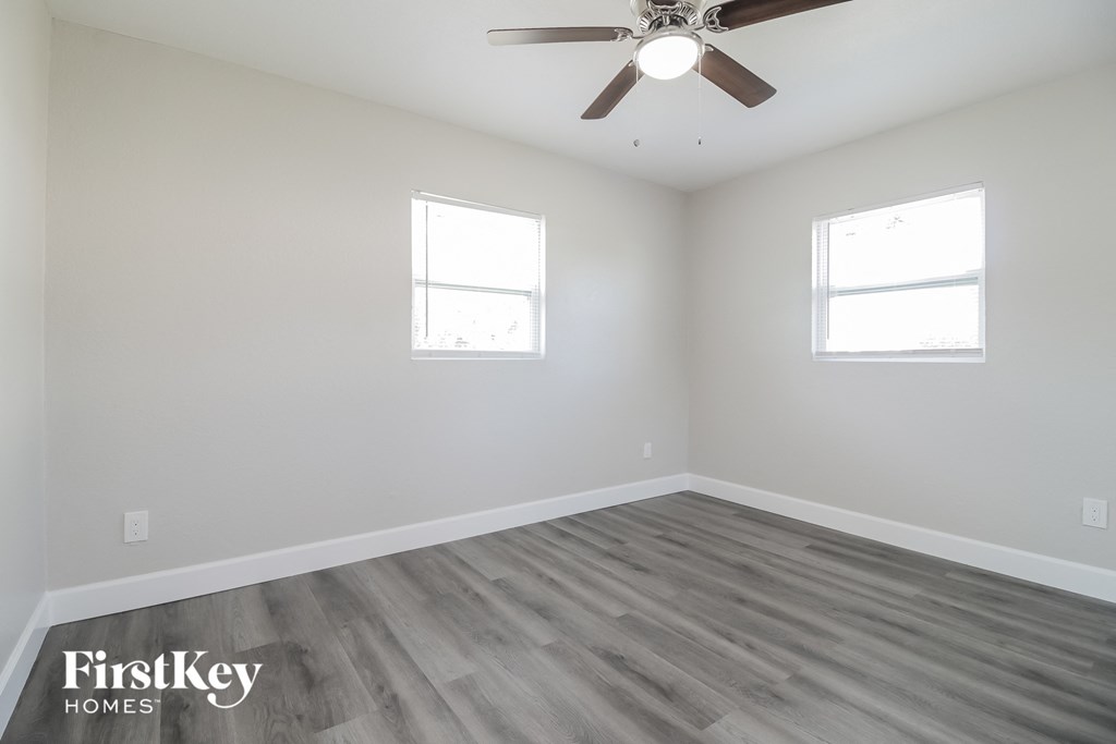 A room with a ceiling fan and two windows.