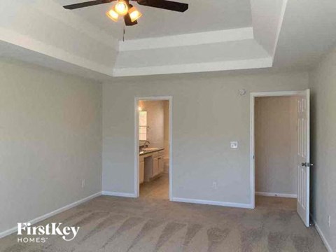 an empty living room with a ceiling fan and a door to a kitchen