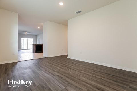 A spacious room with wooden flooring and white walls, with a window on the left side.