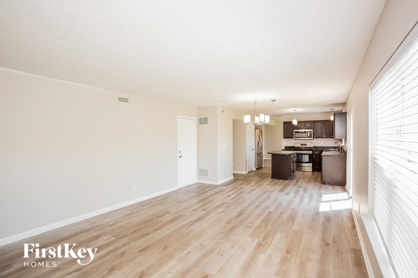 A spacious living room with wooden floors and a kitchen in the background.