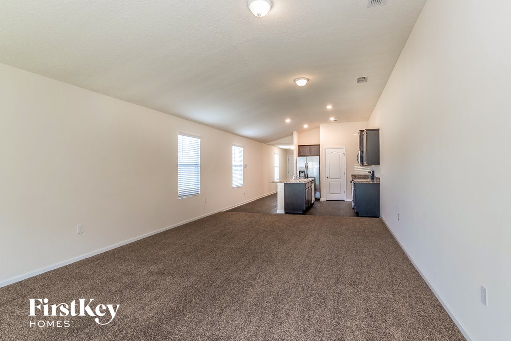 A spacious room with a carpeted floor and a kitchenette in the corner.