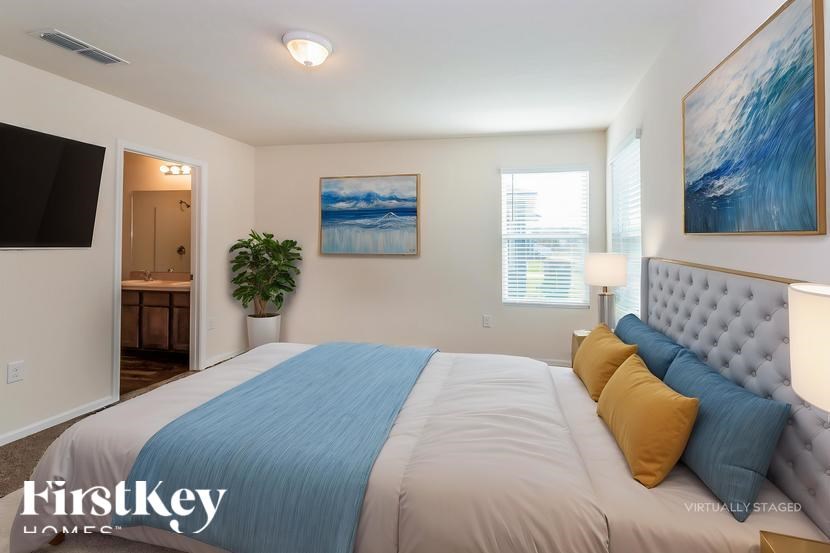 A bedroom with a bed, a plant, and two paintings on the wall.