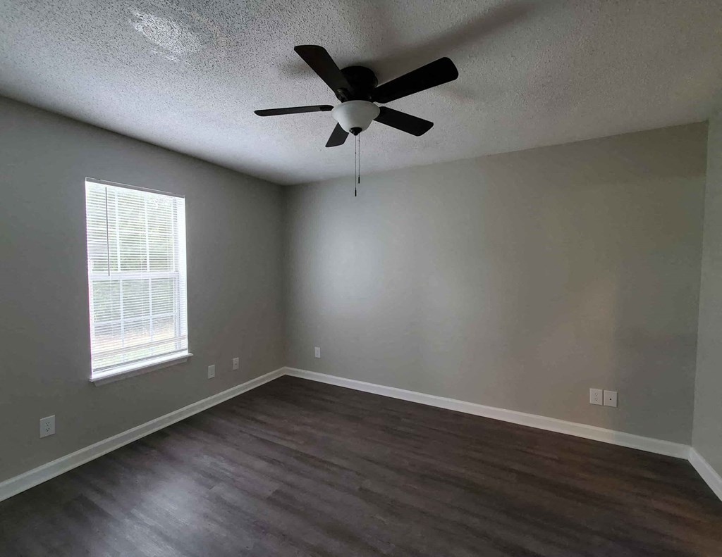 an empty living room with wood floors and a ceiling fan