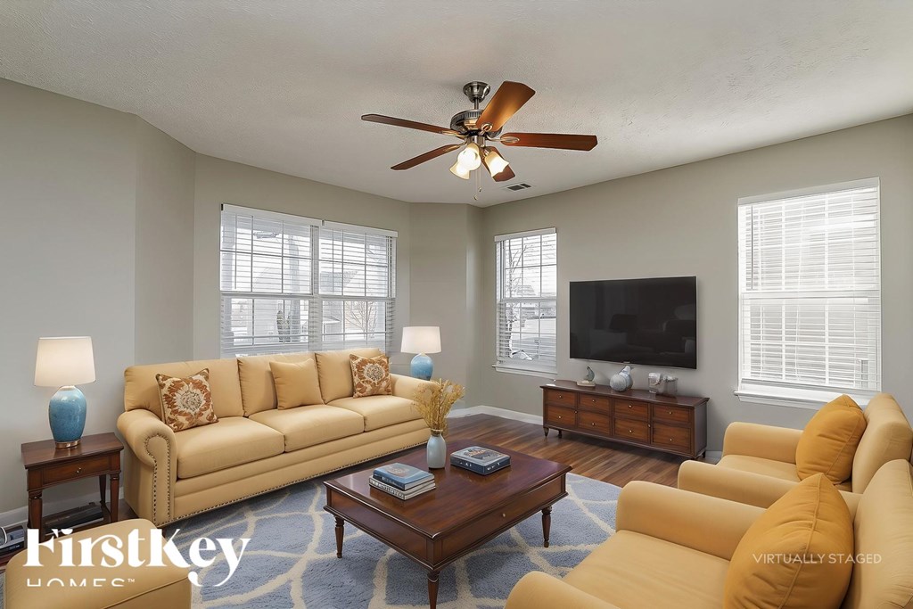 A living room with a tan couch, a coffee table, and a ceiling fan.