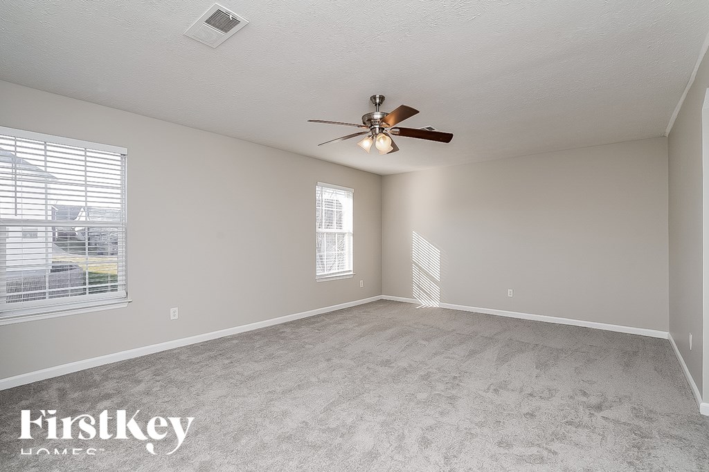 A spacious room with a ceiling fan and two windows.