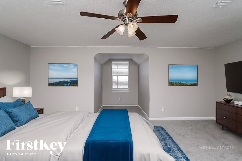 A bedroom with a bed, a ceiling fan, and two pictures on the wall.